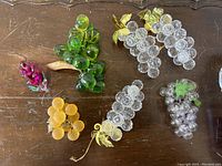 Seven pieces of lucite grape bunches in different colors and leaf styles on a wooden surface, showing full lot contents.