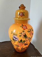 Front view of the illuminated temple jar lamp showing floral enamel design on orange glass.