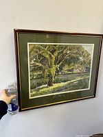 Full front view of the framed watercolor painting with a hand and bottle for scale.