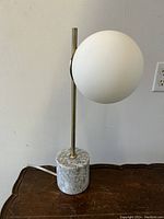 Front angle side view showing marble base, brass vertical rod, and white spherical glass shade.