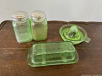 Full shot showing set of green Depression glass butter dish with lid, salt and pepper shakers, and Vaseline glass reamer juicer.
