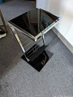 Side view of the chrome modular table showing the black glass top and magazine rack below