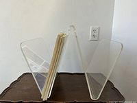Front view of the Lucite magazine stand displaying its transparent V-shaped structure and angled sides to hold magazines or books.