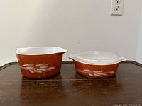 Front view of two Pyrex Autumn Harvest Wheat casserole bowls side by side, one with clear glass lid and one without lid