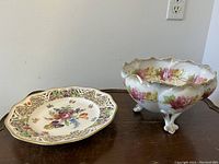 Two porcelain items on wooden surface: a pierced Dresden cabinet plate and a footed bowl with floral motifs.