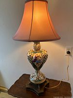 Full view of the lit vintage Italian pierced porcelain table lamp with fabric shade on a wooden table.