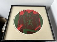 Front view of framed circular serigraph print showing abstract two figures in red, green, and burgundy hues with cream matting and black frame.