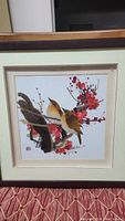 Full view of framed silk tapestry depicting two birds on a flowering branch with red blossoms.