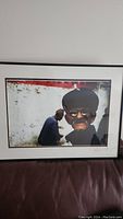 Framed photographic print showing close-up portrait of elderly man with cap and glasses, signed by artist