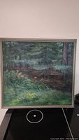 Full view of the framed painting showing a forest landscape with greenery and orange flowers.
