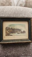 Framed miniature watercolor painting featuring a rocky coastal landscape with a lighthouse.