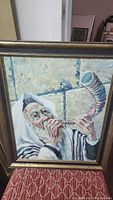Framed oil painting showing a man wearing a tallit blowing a shofar horn.