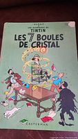Front cover of the comic book showing Tintin and other characters with green background and title Les 7 Boules de Cristal