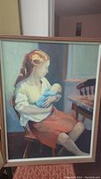 Full view of the framed oil painting showing a woman in a white blouse and orange skirt holding a baby dressed in blue, sitting on a wooden chair.