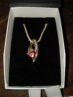 Front view of the pendant in a black box showing red garnet and diamond setting