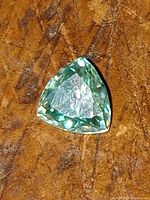 Close-up image of the blue moissanite gemstone on a textured brown background, showing its trillion cut and color.