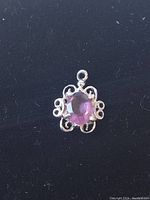 Close-up image of a sterling silver pendant with an oval purple amethyst oval stone surrounded by decorative swirling silver design.