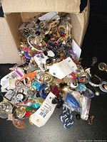 Top view of a box filled with assorted costume jewelry pieces including earrings, bracelets, and brooches spilling from a cardboard box.