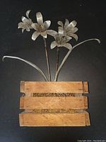 Full view of metal daffodil flower sculpture with wooden base showing three flowers and leaves.