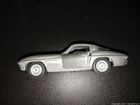 Side view showing the driver's door open, revealing interior detail and wheel design, with silver paint and body vent lines visible.