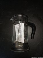 French press coffee maker, clear glass with black plastic handle and base, showing plunger and mesh filter inside.