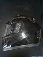 Side view of glossy black full-face helmet showing clear visor and slight wear.