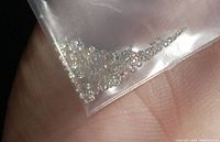 Close-up of numerous small round brilliant moissanite stones held loosely in a small transparent plastic bag, showing their sparkle and quantity.