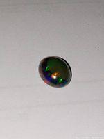 Close-up image of oval cabochon black opal showing green and red play of color on dark body tone.