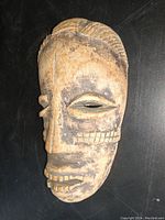 Front angled view showing the carved wooden mask with textured eyebrows, carved eyes, nose, and mouth with worn teeth and patina.