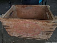 Front side view of the wooden crate showing faded red stamped logo and hand hole cutouts