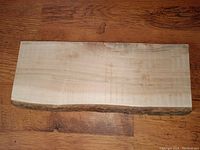 Top view of solid maple slab with natural live bark edge on one side, smooth sanded surface on top.