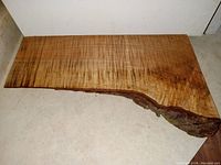 Full view of the front finished side of the tiger maple burl charcuterie board showing wood grain, thickness, and natural edge with bark.