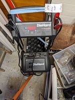 Front and top view of the DieHard battery charger and engine starter showing brand, digital display, and cables.