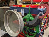 Photo showing green block pulley with red hook attached to a metal frame, with large metal sifter placed beside it
