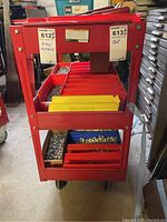Front view of red metal rolling cart loaded with red and yellow divided plastic bins containing small hardware items.