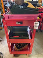 Front view of red US General service cart showing three shelves with pink and green trays containing tools and hardware.