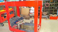 Front-angle view of red metal wheeled cart showing open frame and contents on bottom shelf (not included)