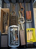 Overview of carving tools, chisels with wood handles, vintage wrenches and other assorted metal hand tools placed in plastic trays and a cardboard box.