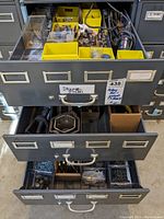 Three open drawers of a black metal cabinet filled with yellow bins containing rotary bits and small hardware