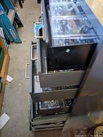 Side view of black metal drawer units containing multiple plastic boxes filled with assorted hardware items such as screws and nuts.