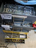 Top view of drawers with clear plastic compartment boxes holding assorted plumbing fittings labeled 'PLUMBING F-LTINGS' and bolts.
