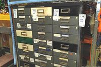 Full front view of multi-colored metal organizer cabinet with 30 drawers, showing labels on several drawers and heavy use wear.