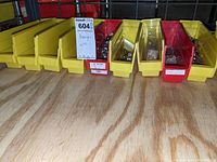View of yellow and red plastic bins with assorted plated nylon lock nuts and fasteners on wooden surface.