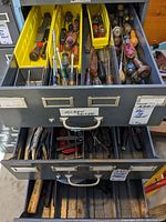 Upper drawer containing various screwdrivers organized in yellow and gray plastic bins, some with wooden handles, others plastic, heavily used condition