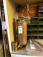 Front view of brass/copper cylindrical vessel with bottom spigot and hanging hook