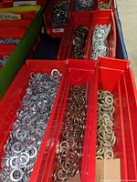 Photo showing multiple red plastic bins filled with silver, brass, and dark steel split lock washers, organized by size and type.