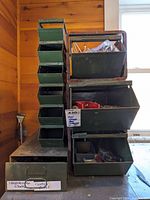 Front view of stacked green steel bins with assorted hardware and tools inside, some containers labeled