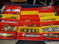 Overhead photo of multiple red and yellow plastic bins filled with various steel washers.