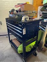 Black US General tool cart with drawers and various items stored on top and below.