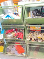 Green metal bins holding assorted welding torches, fittings, springs, and metal parts.